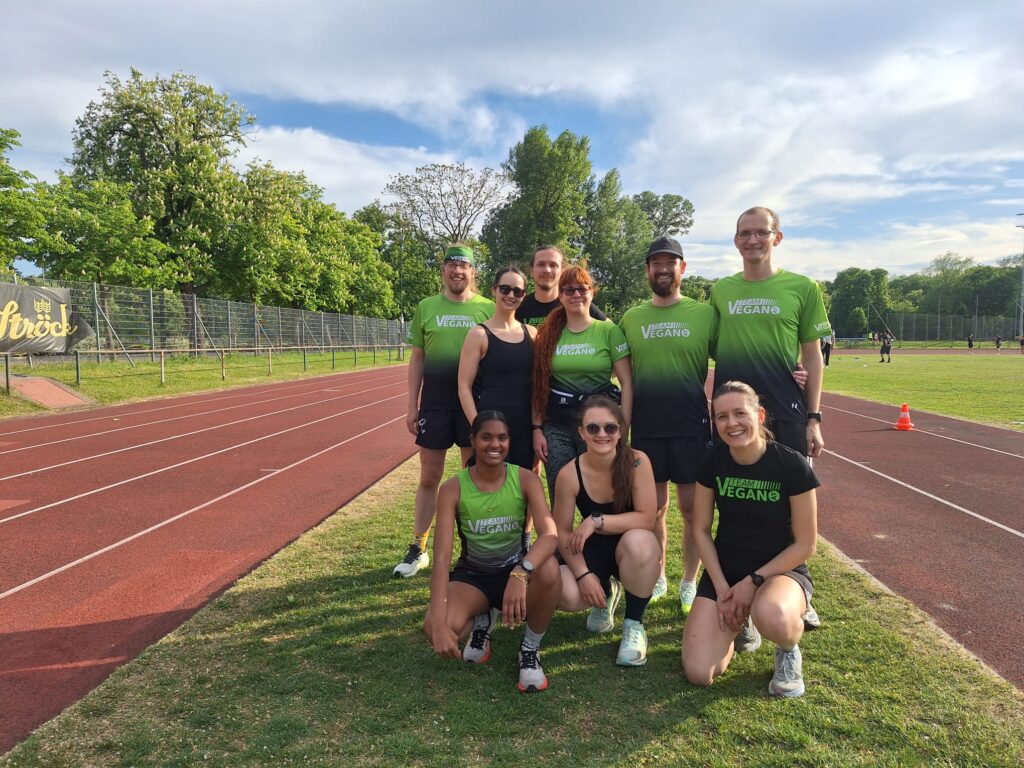 Ein Gruppenfoto beim Lauftraining von Team Vegan im Leichtathletikzentrum. Vier Männer und fünf Frauen sind zu sehen, manche tragen Sportbekleidung von Team Vegan. 
